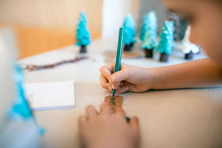Cute girl preparing DIY gifts and signing tags to parents and family for Christmas, a green cone as if it is small toy pine tree, tags and festive boxes, handmade presents, zero waste holidaysの写真素材