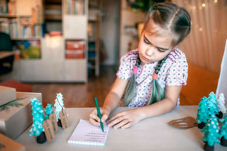 Cute girl preparing DIY gifts and signing tags to parents and family for Christmas, a green cone as if it is small toy pine tree, tags and festive boxes, handmade presents, zero waste holidaysの写真素材