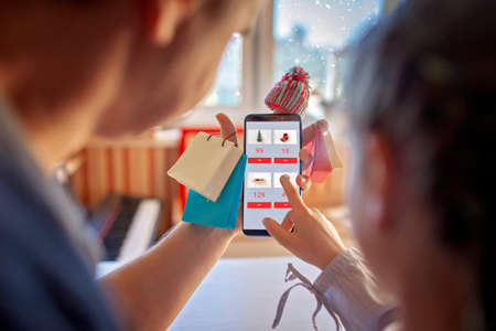 Online shopping concept. Handsome father with his cute daughter having fun with smartphone wearing...