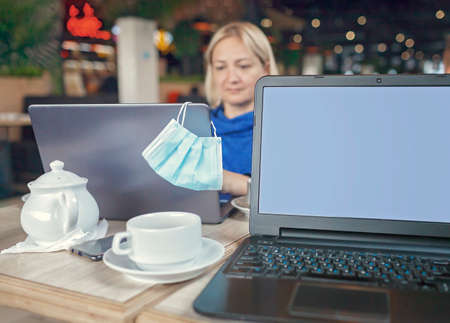 Businesswoman sitting in modern cafe with portable computer and drinking coffee during online meeting, social distance, new reality lifestyleの写真素材