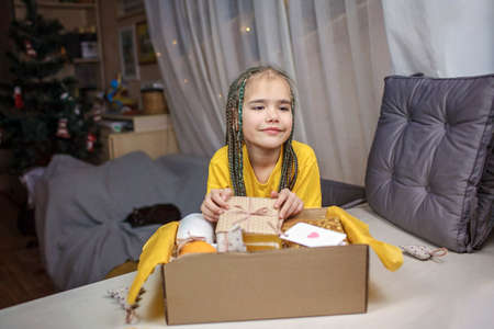 Cute girl packing festive care box with tea, honey, cookies and knitted wool socks for grandmother. Personalized care box during lockdown, support and surprise for family and friends on Christmasの写真素材