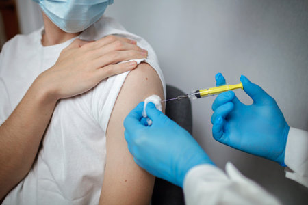Close up shot of doctor in medical mask and gloves holding ampoule with coronavirus vaccine, nurse...