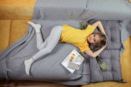 Cute girl in yellow t-shirt lying on bed with grey blanket, enjoying cookies and cacao, dreaming without gadget, digital detox, slow living, top view shot in colors of year 2021, indoor lifestyleの写真素材