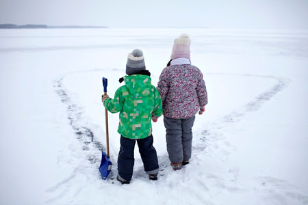 Boy and girl have fun and removing snow from the ice on the frozen lake in heart shape. Winter romantic, silence and wild nature, active winter weekend, outdoor activities, icy landscape, lifestyleの写真素材