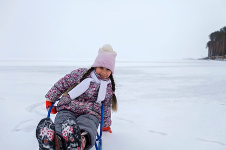 School age girl have fun on the frozen lake and enjoying a sleigh ride. Winter, silence and wild nature, active winter weekend, seasonal outdoor activities, happy family lifestyle, copy spaceの写真素材