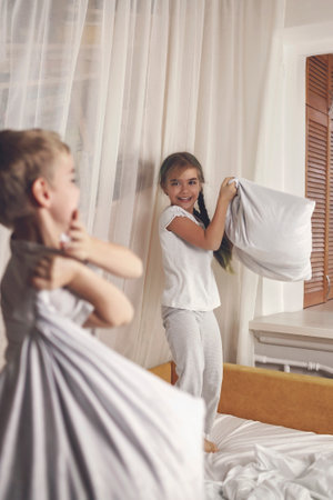 Happy little kids in pajamas staged a pillow fight in bed in the bedroom, healthy sleeping, invest in rest conceptの写真素材