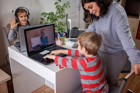 Distant education at home, children doing homework and mother working and help them. Elementary school kids during online class with parent working remotely in one room, self-isolation, quarantineの写真素材