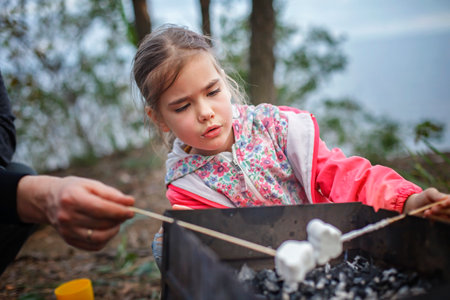 New normal escape step, wild nature walking and family outdoor recreation. Kids cooking and tasting marshmallows fried on fire, hike at weekend, lifestyleの写真素材