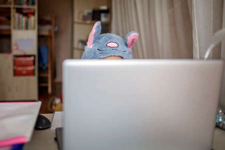 Distant education, online class meeting. Pretty schoolgirl wearing funny rabbit hat with ears to amuse classmates during boring online lesson at home, social distance during quarantine, self-isolationの写真素材