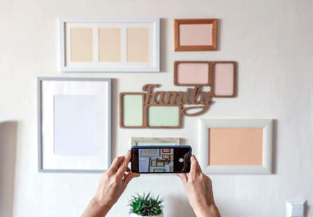 Woman making photo of white wall with set of different empty vertical and horizontal picture frames, family photo gallery project to capture moment, mockup template on the white background, lifestyleの写真素材