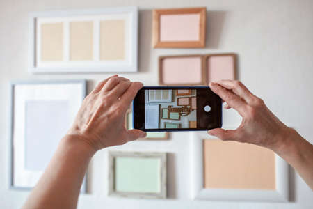 Woman making photo of white wall with set of different empty vertical and horizontal picture frames, family photo gallery project to capture moment, mockup template on the white background, lifestyleの写真素材