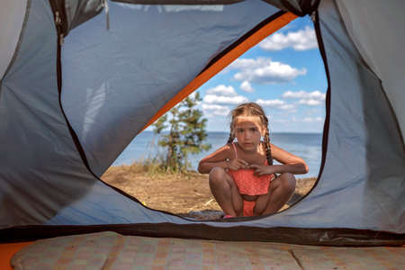 Kid looking into the tent at campsite on the beach among wild forest, active lifestyle, family recreational weekend, happy summertime, stay and explore local, outdoorの写真素材