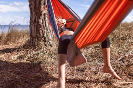 Cute girl having rest in hammock in the wild forest during local vacation, family summer weekend, social distance, unity with nature, digital detox, active lifestyleの写真素材