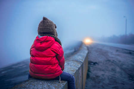Cute 7 years old girl walking alone on the road in spring foggy day, uncertainty and looking forward concept, lifestyle outdoor. Stress, depression and psychological problem of isolationの写真素材