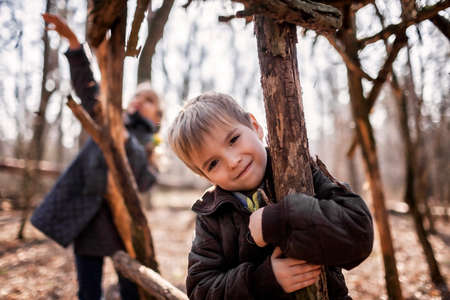 Young adventurers, boy and girl, building a wooden habitat in the wild forest during their social distant walking in lockdown time, walking on fresh air, outdoor active lifestyleの写真素材