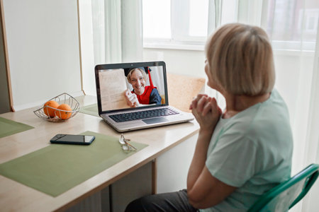 Virtual graduation and convocation ceremony. Senior woman congratulating her daughter in graduation gown and cap during online video call, distant education andの写真素材
