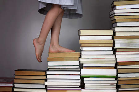 Preschool girl going up the stairs of books from one education level to another, studio shot, study and education conceptの写真素材