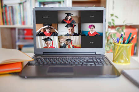 Virtual graduation and convocation ceremony. Laptop screen with happy students wearing graduation gown and cap receiving congratulation during online video call, distant educationの写真素材