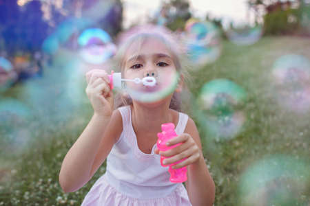 A little girl blowing soap bubbles in summer park, happy childhood, healthy outdoors lifestyle,...