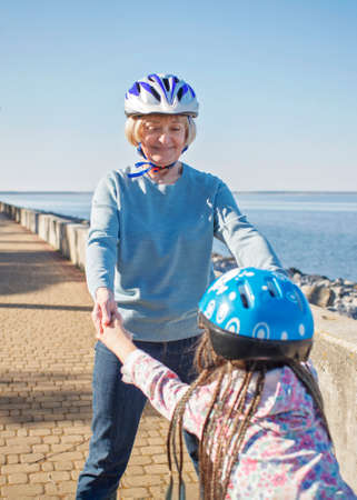 Happy girl with her grandmother riding on roller skates together at park, hugs and support, active family activity, spring outdoors, healthy lifestyle,の写真素材