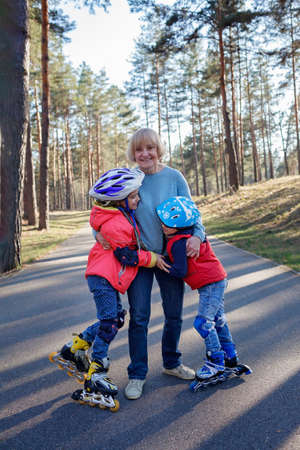 Happy kids riding on roller skates together with grandmother at park, hugs and support, active...