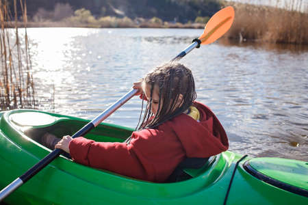 Happy preteen girl kayaking alone on the river, paddle in the hand, summer camp activity, extreme sport, outdoor lifestyleの写真素材
