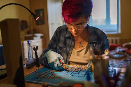 Geek teenage girl in protect eyeglasses engineering an airplane model at home, generation Z...