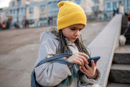 Preteen girl sitting on street stairs and texting with smartphone on way from shopping, trendy schoolgirl with grey mesh eco bag with purchase, yellow fruits, zero waste, sustainable lifestyle conceptの写真素材