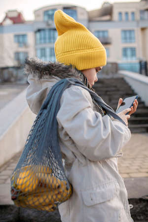 Teenager girl texting with smartphone on street stairs on way from shopping, trendy schoolgirl with...