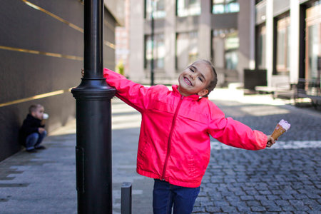 Pretty little girl in pink coat eating an ice-cream in the city street, spring outdoor lifestyleの写真素材