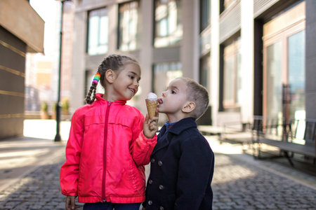 Pretty little girl with her younger brother eating an ice-cream in the city street, spring outdoor lifestyleの写真素材