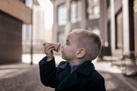 Funny kid eating ice cream at street over urban background, little candy boy have fun and hold waffle cone like a beak of bird, sweet dessert, street food, outside lifestyleの写真素材