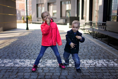 Pretty little girl with her younger brother eating an ice-cream in the city street, spring outdoor lifestyleの写真素材