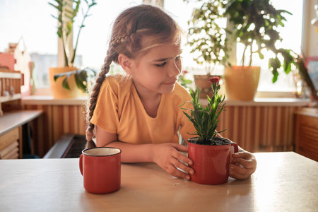 Preteen girl drinking coffee and enjoying green blooming flower replanted in usual red mug, home floral decor, home gardening and slow living concept, potted green plants at homeの写真素材