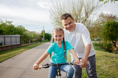 Father teaching her little daughter to ride a bicycle, happy summer in village, healthy lifestyle, childhood, fatherhood and upbringing, concept for father dayの写真素材