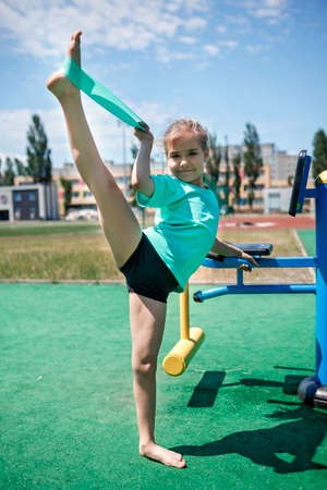 Cute preteen girl making exercises with fitness resistance band at public sportsground in the city, wellness and fitness, sport and recreations, healthy lifestyleの写真素材