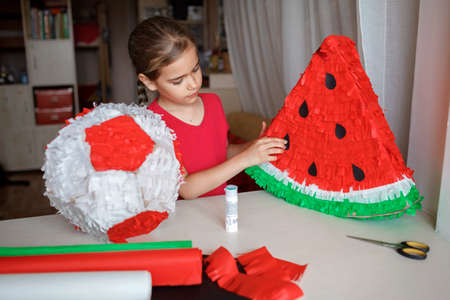 Preteen girl doing pinata with cardboard from used box and color crepe paper, decorated container filled with candy as a part of celebration, diy decoration at birthday, bright idea for kids activityの写真素材
