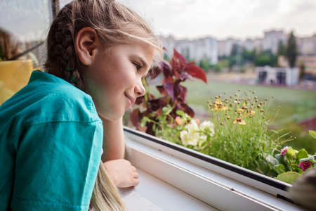 Cute girl helping to care for home plants on the balcony window, plant parents concept, home gardening, green environment, nature and ecology at homeの写真素材