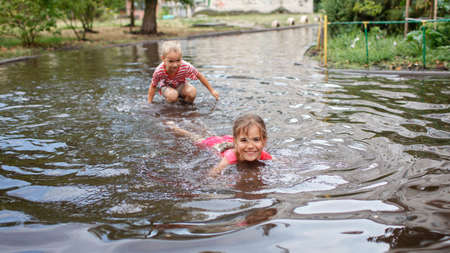 Cute kids jumping and swimming in the puddles after warm summer rain, outdoor walking in any weather, happy childhood and summertime, healthy lifestyleの写真素材