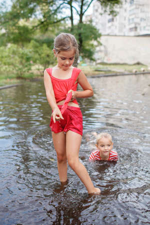 Cute kids jumping and swimming in the puddles after warm summer rain, outdoor walking in any weather, happy childhood and summertime, healthy lifestyleの写真素材
