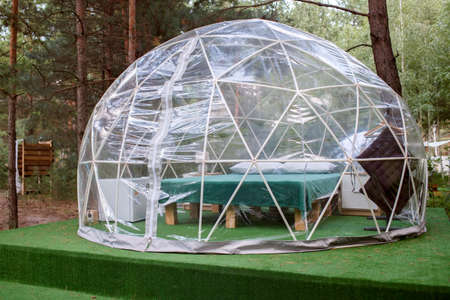 Transparent bell tent with comfortable bed and pillow in forest, glamping hotel, luxury travel,...