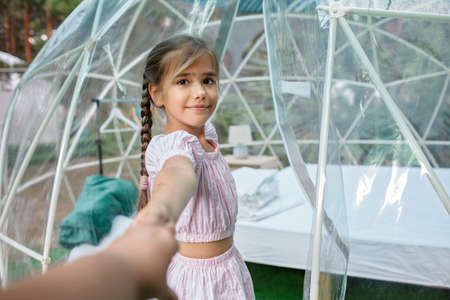 Cute girl looking through transparent bell tent with comfortable bed in forest, glamping hotel,...