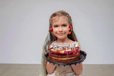 Preteen girl with cherry on the ears holding birthday cake with candles and blowing them out over white pastel background, birthday celebration party, close-up portrait, studio shotの写真素材