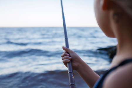 Pretty girl in swimming wear fishing from sea beach in early morning, blue hours, active weekend and camping, outdoors lifestyleの写真素材