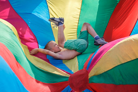 Happy boy having fun and waving in the center of bright colorful parachute, outdoors party, summer...