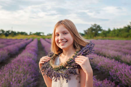 Teenage girl enjoys the scenery of lavender field. Dreamy teenager with floral wreath walking among purple flowers. Calm landscape, escape to beauty of nature, summer lifestyleの写真素材