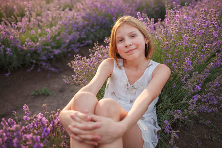 Teenage girl enjoys the scenery of lavender field. Dreamy teenager sitting among purple flowers. Calm landscape, escape to beauty of nature, summer lifestyleの写真素材