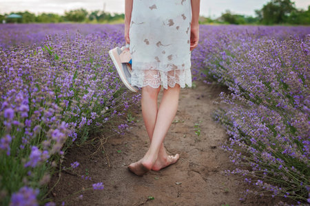 Teenage girl enjoys the scenery of lavender field. Dreamy teenager walking among purple flowers. Calm landscape, escape to beauty of nature, summer lifestyle, back viewの写真素材