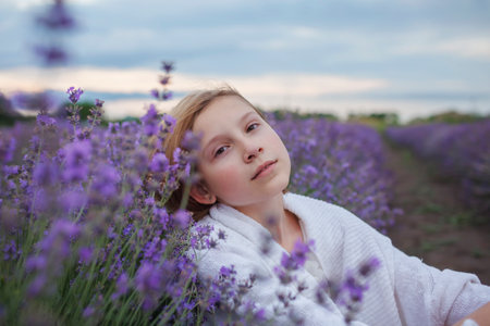 Teenage girl enjoys the scenery of lavender field. Dreamy teenager sitting among purple flowers. Calm landscape, escape to beauty of nature, summer lifestyleの写真素材