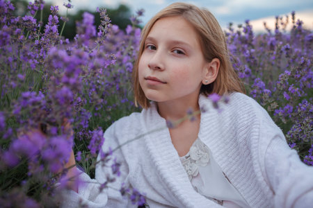 Teenage girl enjoys the scenery of lavender field. Dreamy teenager sitting among purple flowers. Calm landscape, escape to beauty of nature, summer lifestyleの写真素材